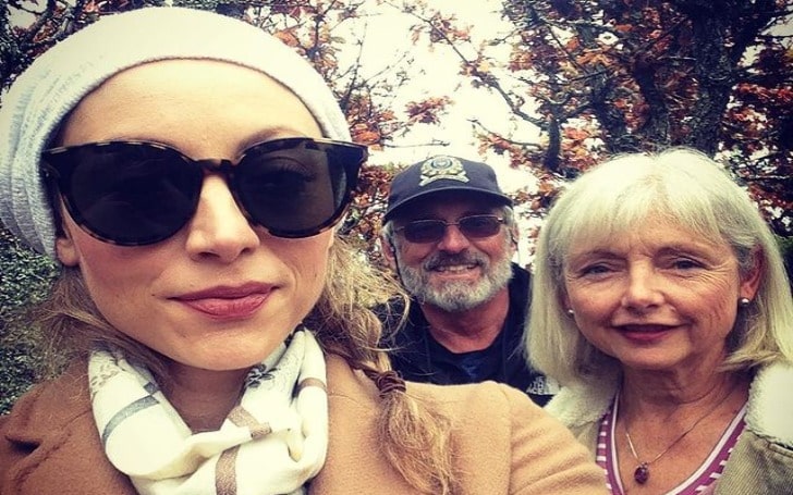 Leah Gibson in a brown jacket, white scarf, black goggles, and white cap with her father and mother.